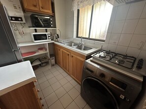 A compact kitchen with a gas stove, microwave, sink, and wooden cabinets. - Oceana Suites Ensenada Villarrica (Villarrica)