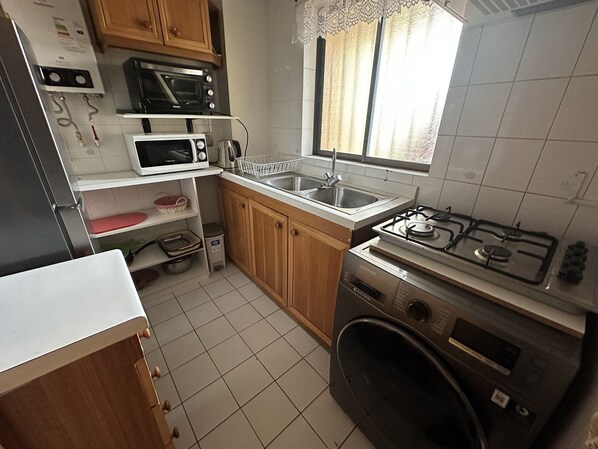 A compact kitchen with a gas stove, microwave, sink, and wooden cabinets.