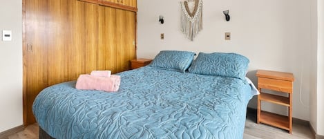 A bedroom with a large bed, wooden wardrobe, two bedside tables, and wall-mounted decor.