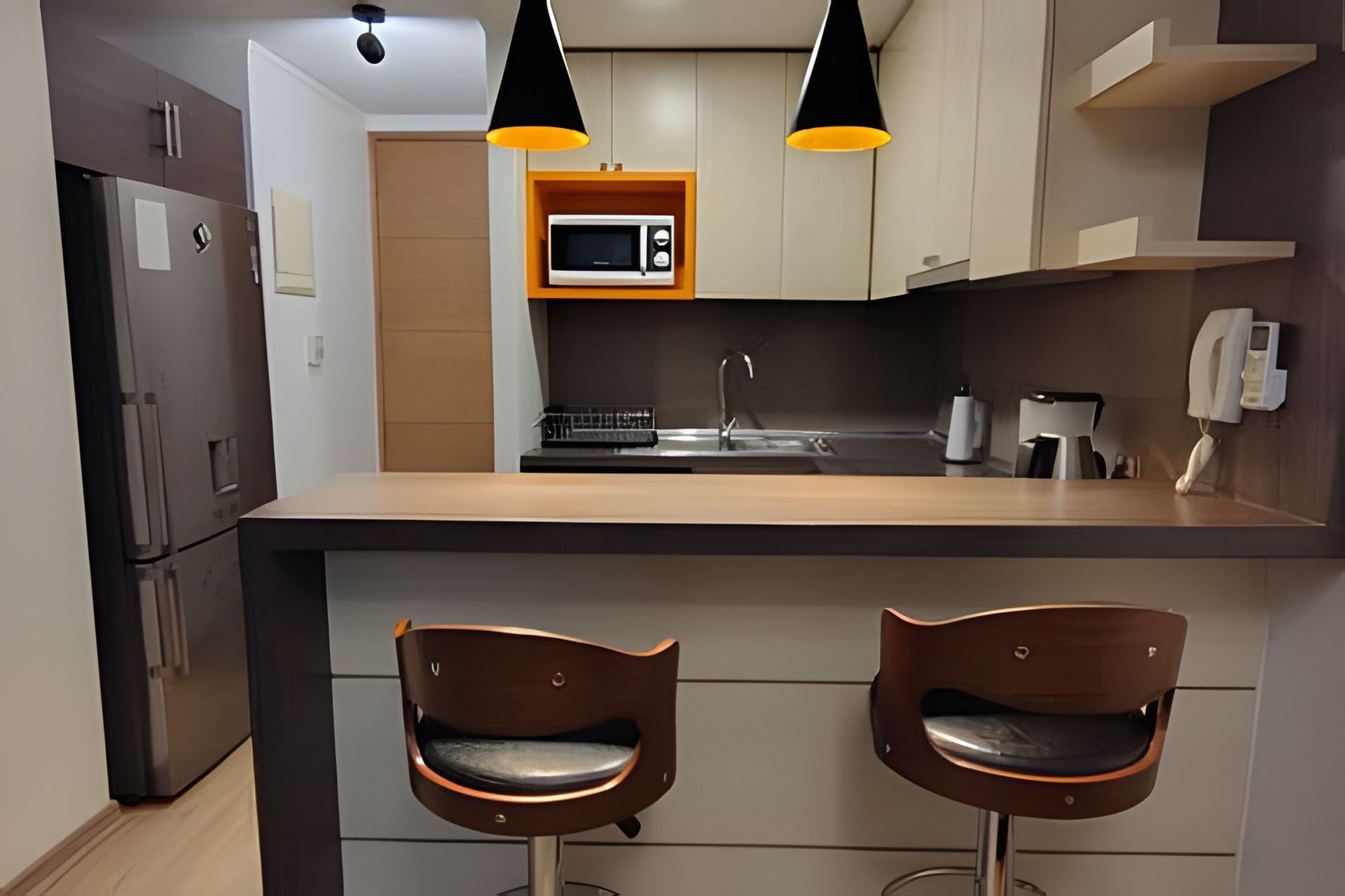 Una cocina moderna con una isla central, dos taburetes de bar, microondas, cafetera e iluminación colgante.