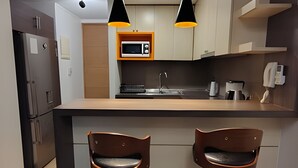 Eine moderne Küche mit einer zentralen Kochinsel, zwei Barhocker, einer Mikrowelle, einer Kaffeemaschine und Pendelleuchten.