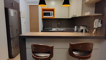 Una cocina moderna con una isla central, dos taburetes de bar, microondas, cafetera e iluminación colgante.