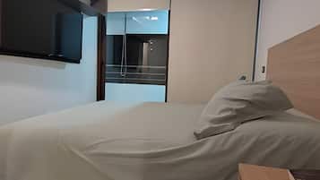 Una habitación de hotel moderna con una cama, un cabecero de madera, un televisor de pantalla plana montado en la pared y una ventana con vistas al cielo.