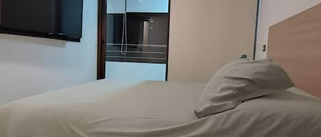 Una habitación de hotel moderna con una cama, un cabecero de madera, un televisor de pantalla plana montado en la pared y una ventana con vistas al cielo.