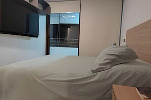 Moderni hotellihuone, jossa on sänky, puinen pääty, seinälle asennettu taulutelevisio ja ikkuna, josta avautuu näkymä taivaalle.