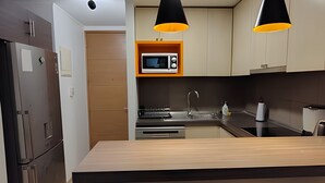 A modern kitchen with a built-in microwave, stainless steel appliances, and black pendant lighting. - Oceana Suites Morandé (Santiago)