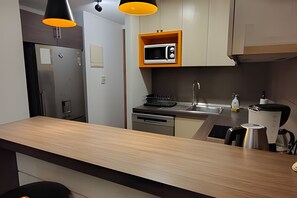 A modern kitchen with a built-in microwave, stainless steel appliances, and a wooden countertop. - Oceana Suites Morandé (Santiago)