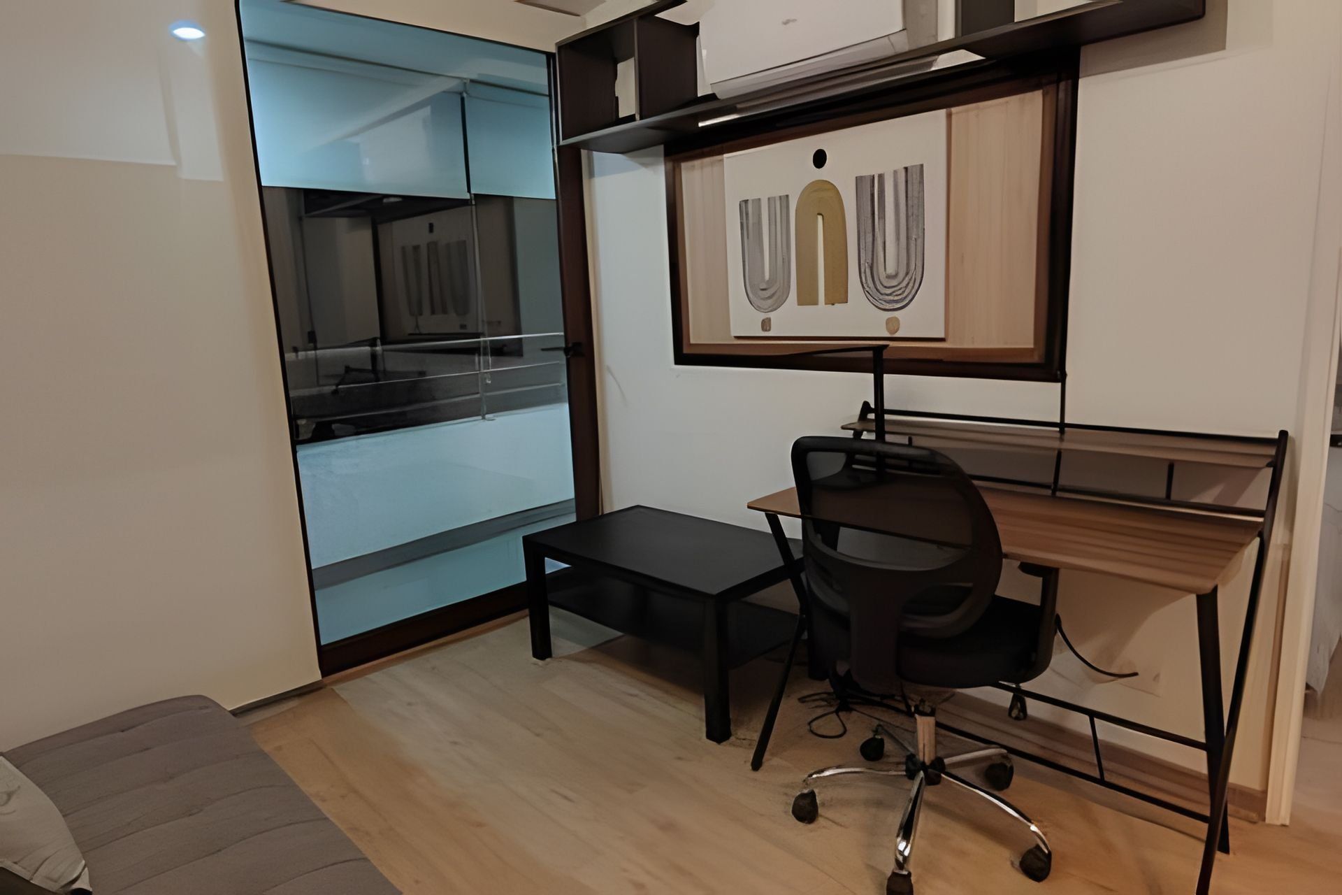 Un pequeño espacio de oficina con un escritorio, una silla y un ventanal grande.
