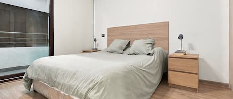 A bedroom with a bed, two bedside tables, a nightstand, and a window.
