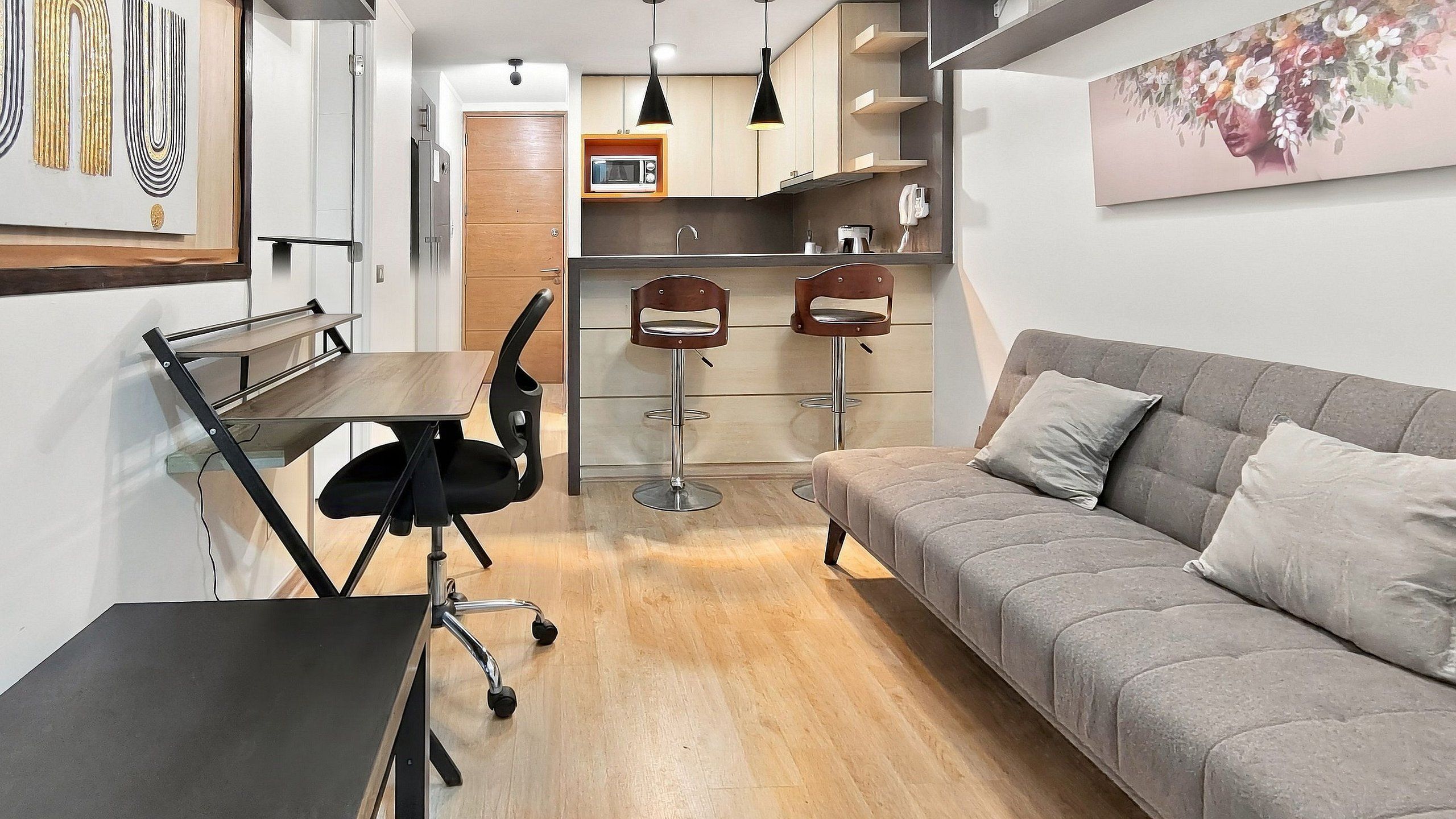 Una sala moderna con un sofá gris, una mesa de comedor con una silla negra y dos taburetes de bar.