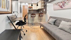 Un salon moderne avec un canapé gris, une table à manger avec une chaise noire et deux tabourets de bar.