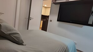 A bedroom with a bed, a TV mounted on the wall, and a door leading to a bathroom. - Oceana Suites Morandé (Santiago)