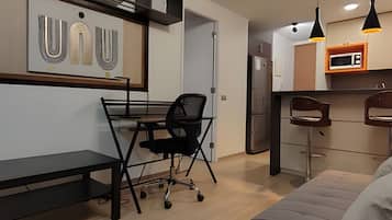 Un espacio habitable moderno con escritorio, sofá, zona de cocina y mesa de comedor.