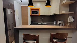 Een moderne keuken met een centraal kookeiland, twee barkrukken, een magnetron, een koffiezetapparaat en hanglampen.