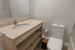 A bathroom with a sink, mirror, toilet, and trash bin. - Oceana Suites Morandé (Santiago)