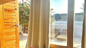 Ein Holztisch mit einer klaren Glasvase voller rosa Blüten, eine Holztür und ein Blick auf eine Terrasse mit Holzmöbeln und einem Baum mit rosa Blüten.