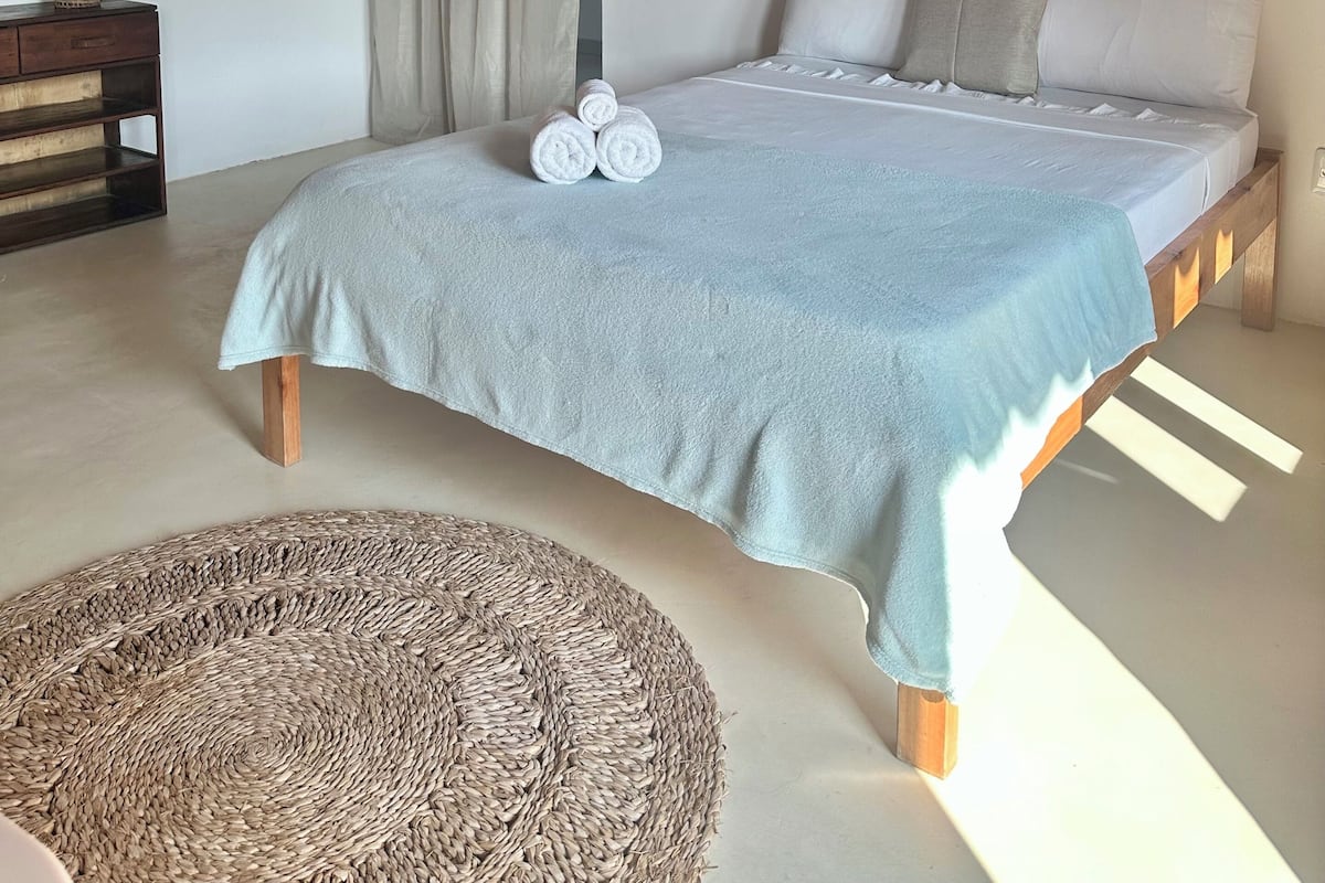 Een slaapkamer met een bed, een hanglamp, een wandairconditioner en een geweven mand op de vloer.