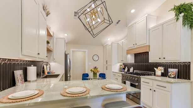 A modern kitchen with white cabinets, a central island with bar stools, a stainless steel stove, and a hanging light fixture.