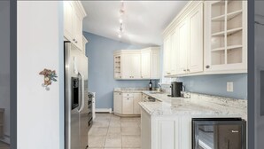 Una cocina con armarios blancos, encimera de mármol y horno empotrado.
