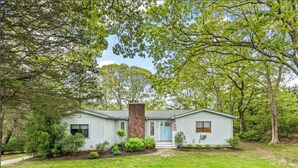 Una casa de un solo piso con chimenea de ladrillo, un porche delantero y un pequeño jardín frontal.