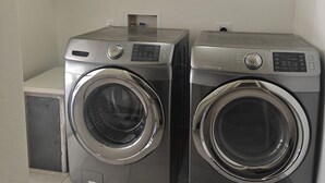 Dos lavadoras de carga frontal en un cuarto de lavandería con un estante blanco encima.