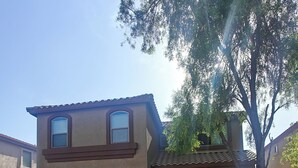 Una casa de dos pisos con una puerta de garaje marrón, un pequeño porche delantero y un árbol en el jardín.