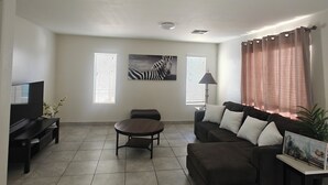 Una sala de estar con una televisión de pantalla plana, un sofá, una mesa de centro y un cuadro en la pared.
