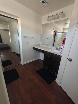 Une salle de bain avec un lavabo blanc, des meubles en bois foncé, un grand miroir et un porte-serviettes orné d’une serviette à motifs.