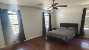 Un dormitorio con cama, ventilador de techo y ventanas amplias con persianas.
