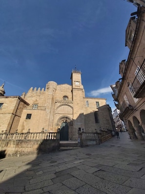 A historic building with a prominent clock tower, arched entrance, and a paved courtyard.