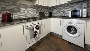 Cocina compacta con gabinetes blancos, microondas, cafetera y lavadora.