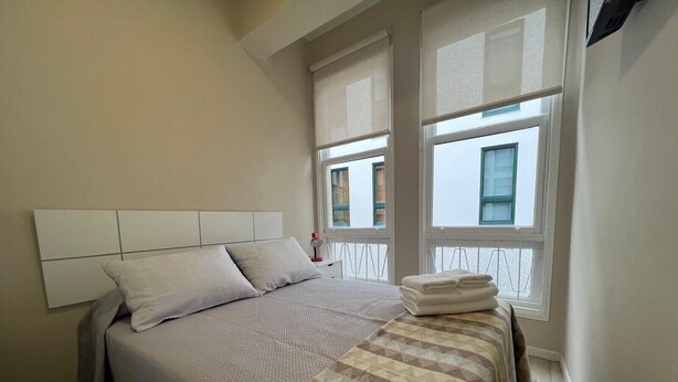 Un dormitorio con cama, dos ventanas y cabecero.
