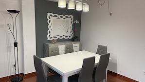 Un comedor con una mesa blanca y sillas grises, una lámpara colgante moderna y un espejo decorativo en la pared.