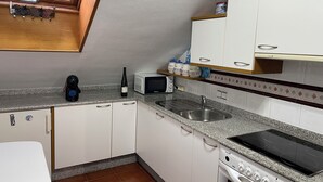 Una cocina con armarios blancos, microondas, botella de vino y cafetera.