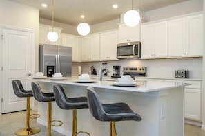 Una cocina moderna con armarios blancos, electrodomésticos de acero inoxidable y taburetes de bar con patas doradas.