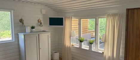 Una habitación con techo de madera, paredes blancas, un armario blanco, un televisor de pantalla plana y una ventana con cortinas.