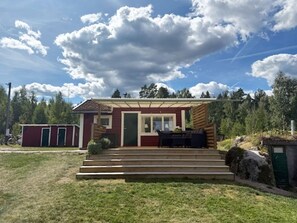 Uma casa térrea com varanda coberta, porta de entrada e um pequeno espaço para sentar ao ar livre.