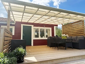 Um alpendre coberto com móveis de exterior, um deck de madeira e uma casa com fachada vermelha e detalhes brancos.
