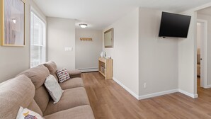 Ein Wohnzimmer mit einer Couch, einem am Wand montierten Flachbildfernseher und einem Flur, der in einen anderen Raum führt.