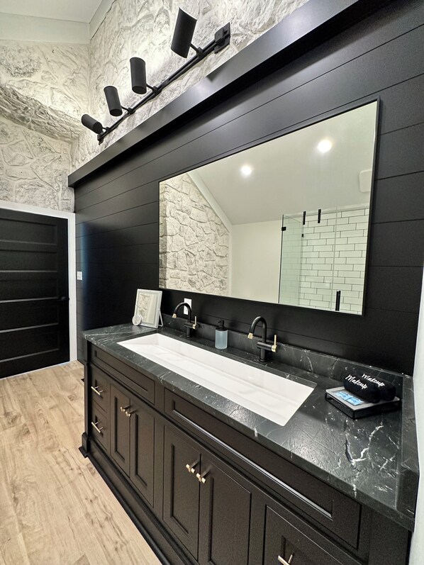 A bathroom with a black vanity, a large mirror, and a stone-textured wall.