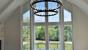 A room with a large bay window, a chandelier, and a view of a green landscape.
