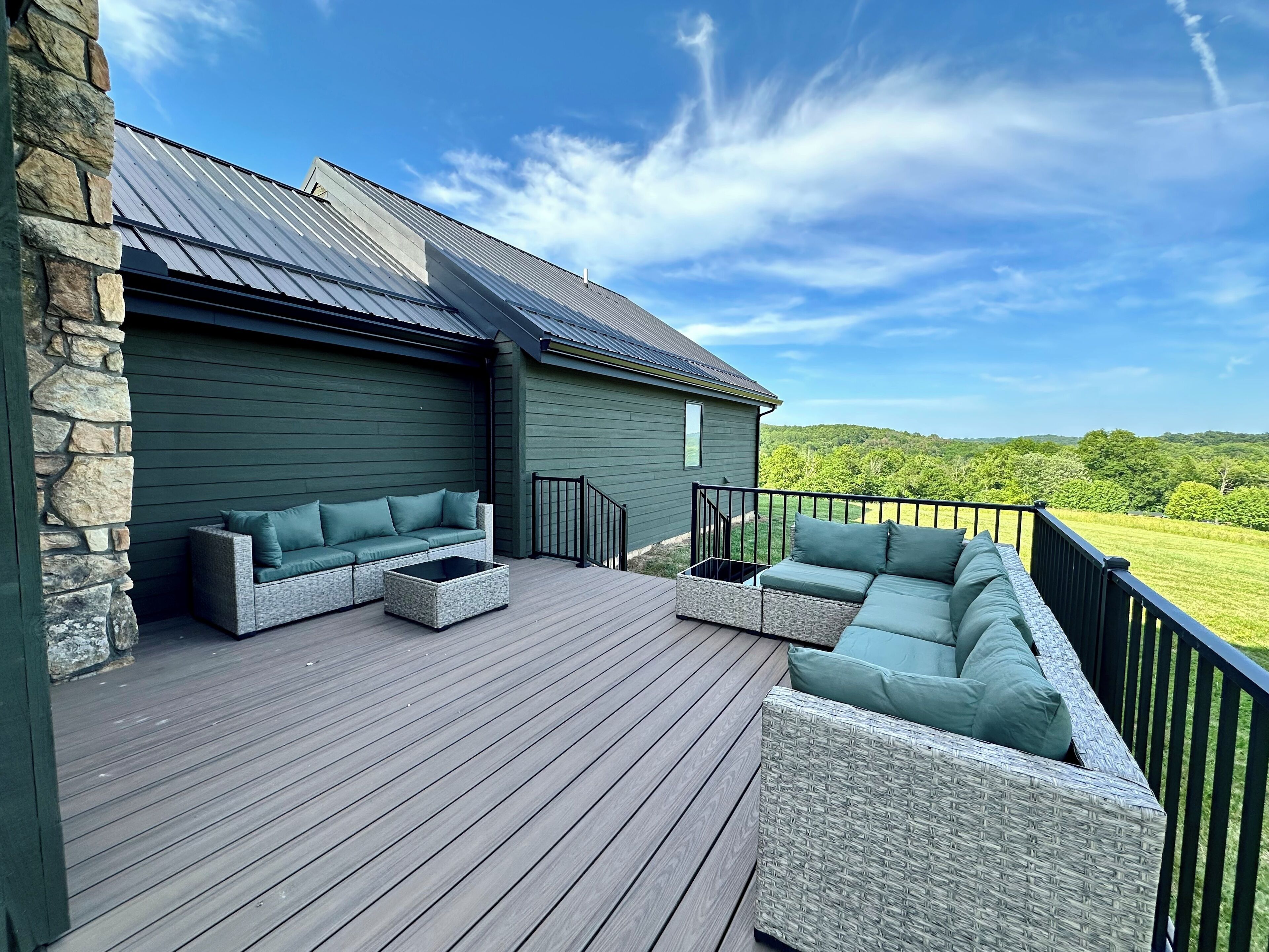 A deck with a stone wall, a green building, and a view of a green landscape.