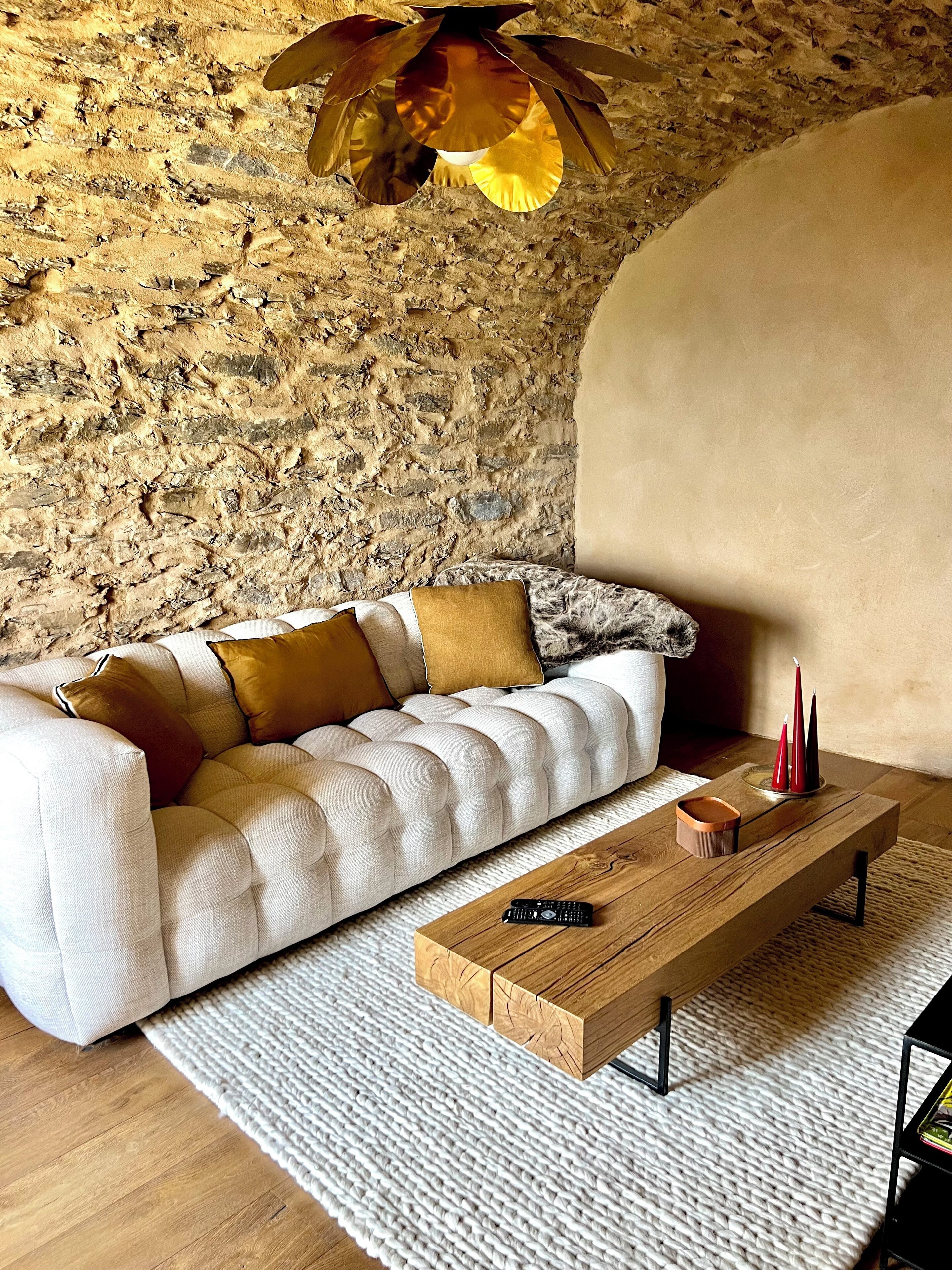 Una sala de estar acogedora con una pared de piedra, un sofá capitonado, una mesa de centro de madera y un control remoto encima.