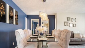 A dining area with a glass table, white upholstered chairs, and a chandelier. - Sunset View House (families) (Calgary)