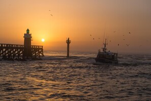 A lighthouse and pier at sunset with a boat in the water.