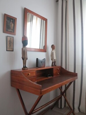 A wooden desk with a mirror, two small figurines, and a black bag.