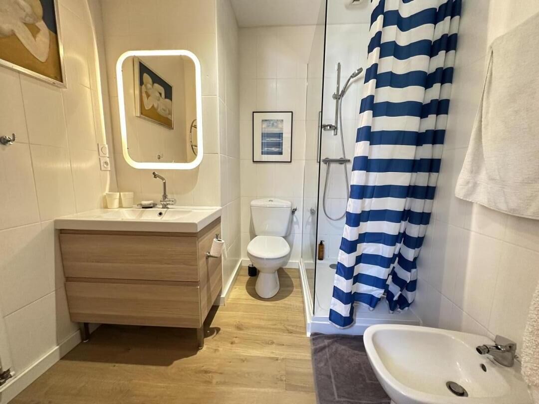 A bathroom with a wooden vanity, a white sink, a toilet, and a shower with a blue-striped curtain.
