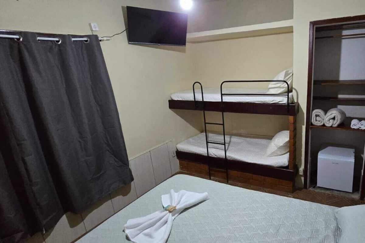 Una habitación pequeña y funcional con literas, un televisor montado en la pared, un armario con estantes y un baño con cortina de ducha.