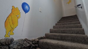 A staircase with a painted wall mural of Winnie the Pooh holding a blue balloon, a stone wall, and a wooden floor.