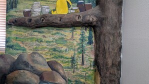 A mural of Winnie the Pooh with jars labeled 'Honey' and 'Honey' on a log, set against a forest backdrop.